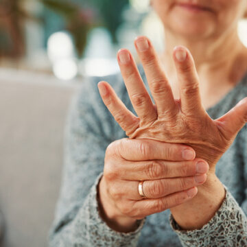 Arthritis, hands or elderly woman on couch with touch, joint pain or stiffness in finger movement. Tendinitis, space or senior person in house with ache, inflammation or hurt muscle in nursing home.