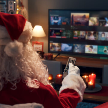 Santa Claus relaxing on the couch at home and watching TV, he is choosing a movie on the video on demand menu
