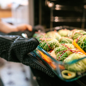 Unrecognizable woman wearing oven mitts glove putting cabbage rolls into oven for christmas dinner in the kitchen. Close-up of a female preparing traditional meal for Christmas eve dinner putting stuffed cabbage rolls into the oven.