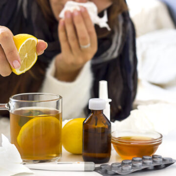 a young unrecognaseble woman with a cold or flu laying on the bed and preparing tea with lemon. Alternative medicine, home treatments and seasolan illnesses concept