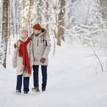 Full length portrait of happy senior couple enjoying walk in winter forest and looking at each other, copy space