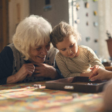 Old woman visit. Multigenerational family get together, grandma, mom and child play chinese checkers in cozy home with warm light, creating loving atmosphere.